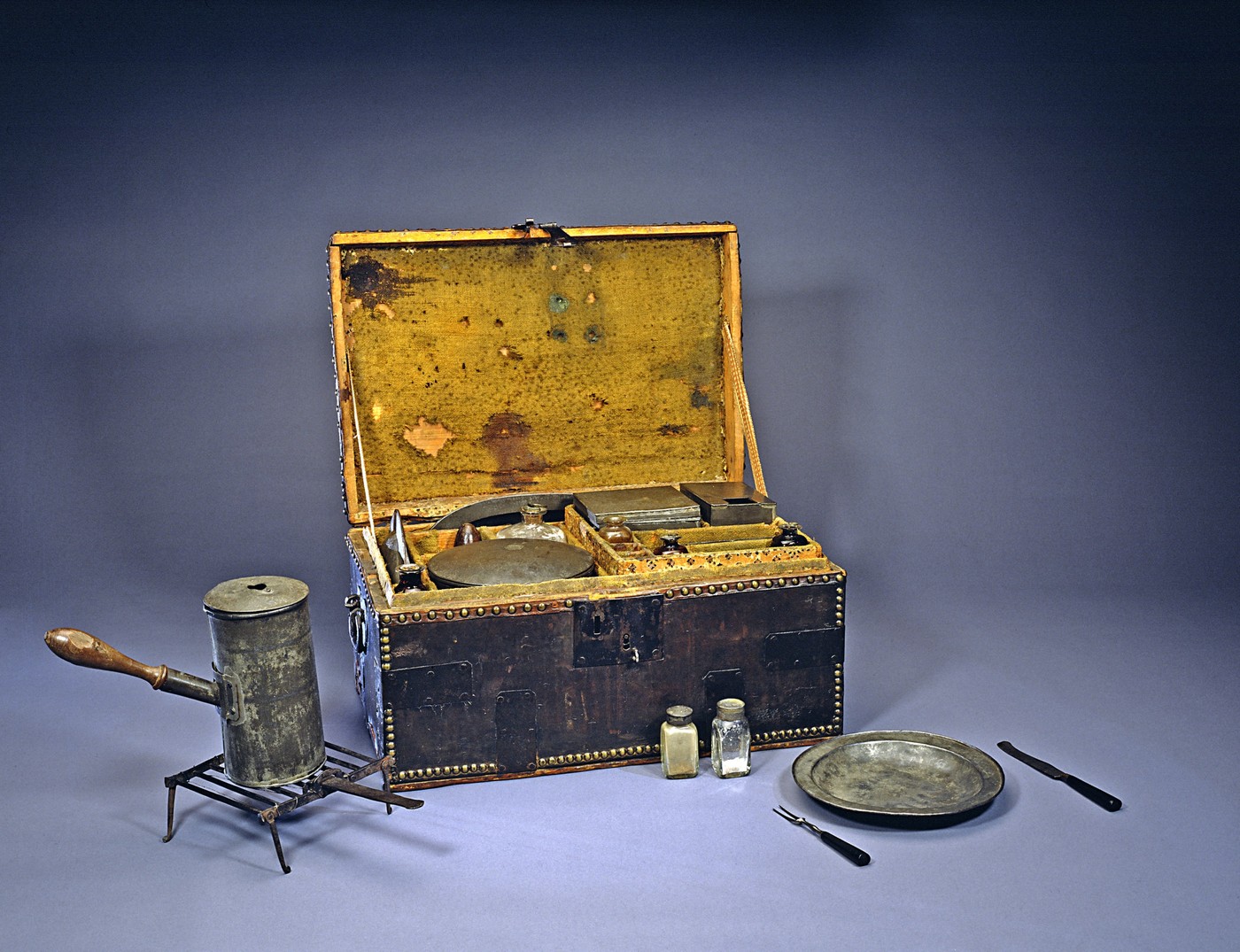 George Washington's Camp Chest containing tin plates and platters, tin pots with detachable wooden handles, glass containers for condiments such as salt, pepper, and sugar, knives and forks with dyed black ivory handles, a tinder box, candle stand, and folding gridiron.